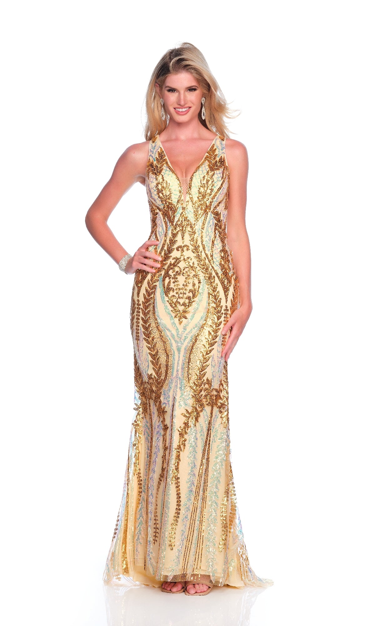 A person stands and smiles in a sleeveless, floor-length Dave and Johnny 12135 gold prom dress with white patterns and a deep V neckline, accessorized with statement earrings, posing against a plain white background.